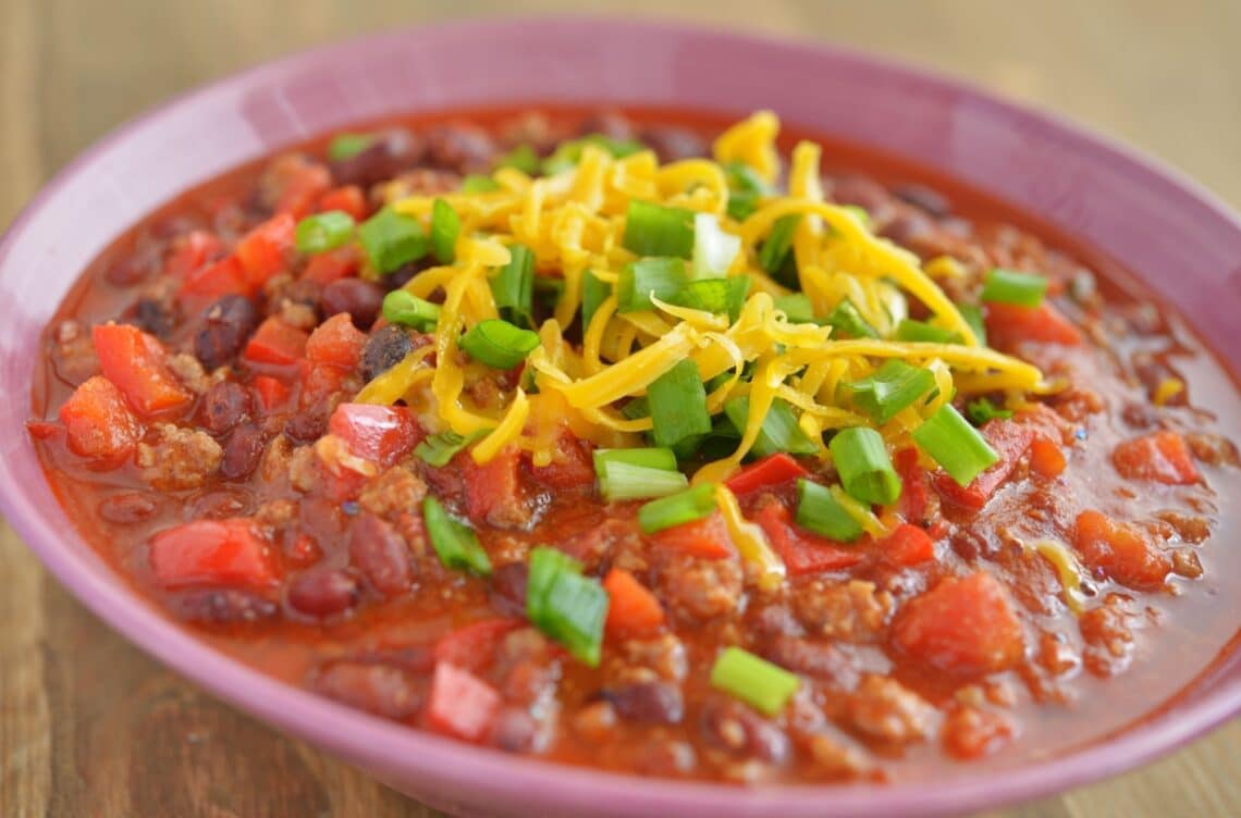 Delicious Venison Chili Recipe In A Red Bowl With Shredded Cheese On Top