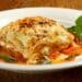 A Slice Of The Most Amazing Meat Lasagna Served On A White Plate With Basil Garnish
