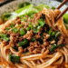 Close-Up Of A Bowl Of Dan Dan Noodles Topped With Spicy Minced Pork, Green Onions, And Sesame Seeds, Served With A Rich, Savory Sauce.